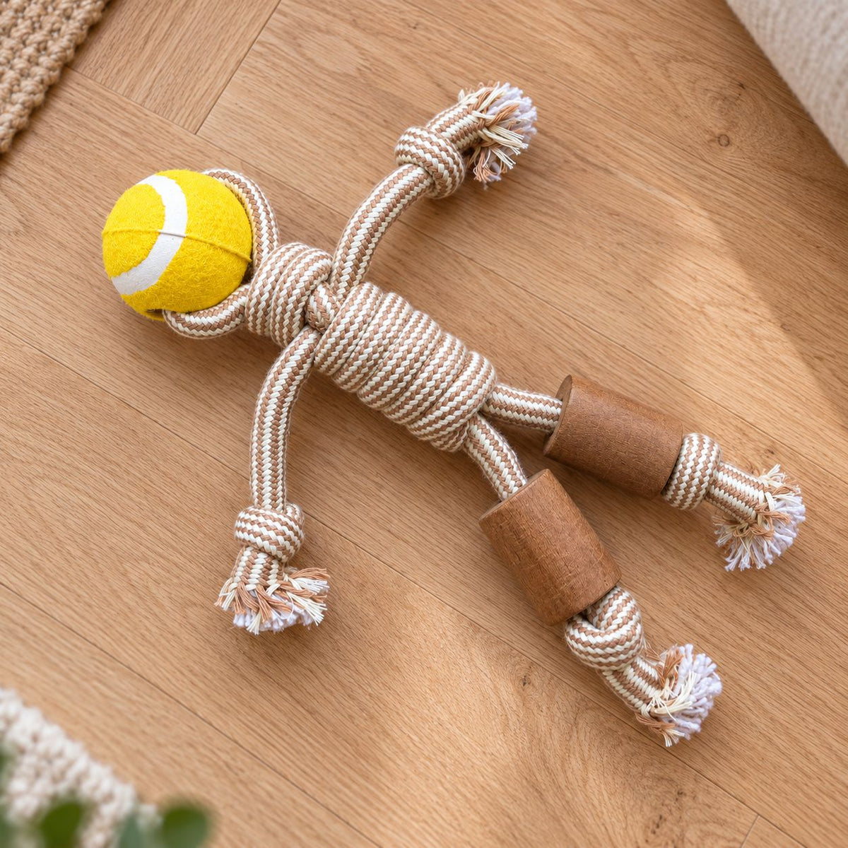 Durable cotton rope dog toy with a yellow tennis ball and wooden rings on a wooden floor.